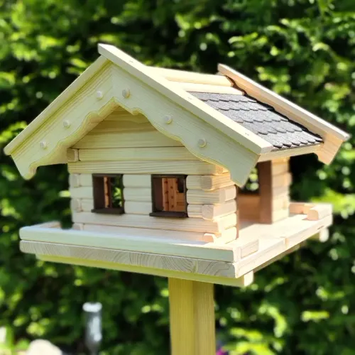 vogelhaus-heidi-mit-grauen-bitumenschindeln -dunkelbraun-gebeizten-tuer-und-fensterzargen-boden-mit-zaun-im-garten